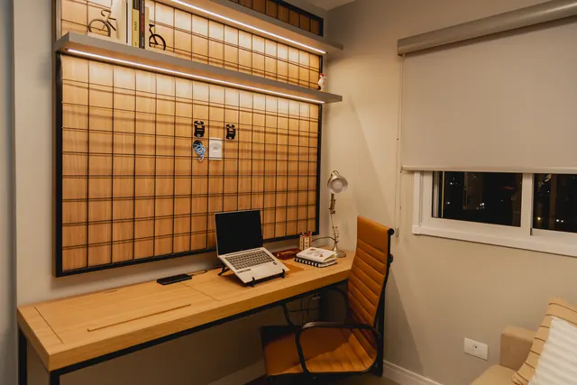 Home office com painel aramado, prateleira iluminada e escrivaninha em madeira